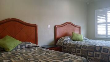 Dos camas individuales con ropa de cama estampada, un cabecero de madera y una ventana con persianas.