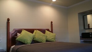A bed with a wooden headboard and green pillows, a bedside table, and a wall-mounted TV. - Travel Inn (Oakland)