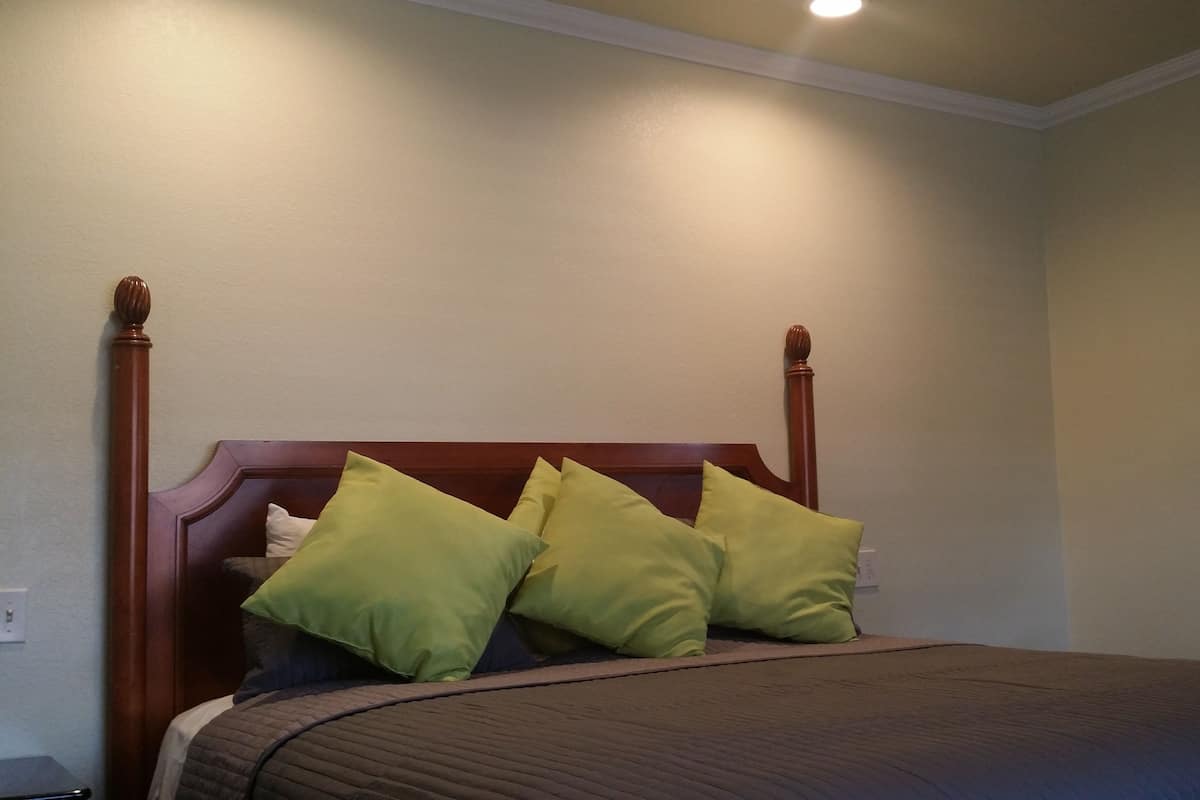 A bed with a wooden headboard and green pillows, a bedside table, and a wall-mounted TV.