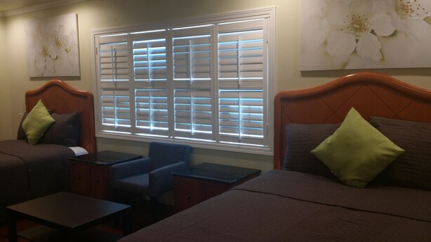 A hotel room with two beds, a small table, and a window with blinds. - Travel Inn (Oakland)