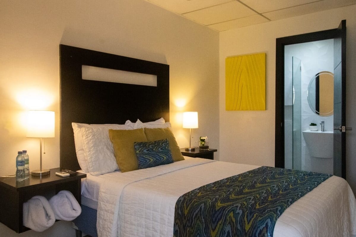Une chambre d’hôtel comprenant un lit, deux tables de chevet, une commode, un miroir et une porte.