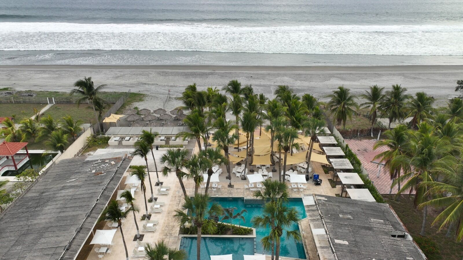 A resort with a swimming pool, beach view, and palm trees.