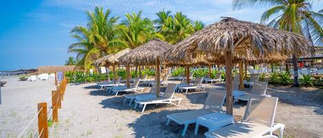 A beach with thatched umbrellas and white lounge chairs arranged in rows.