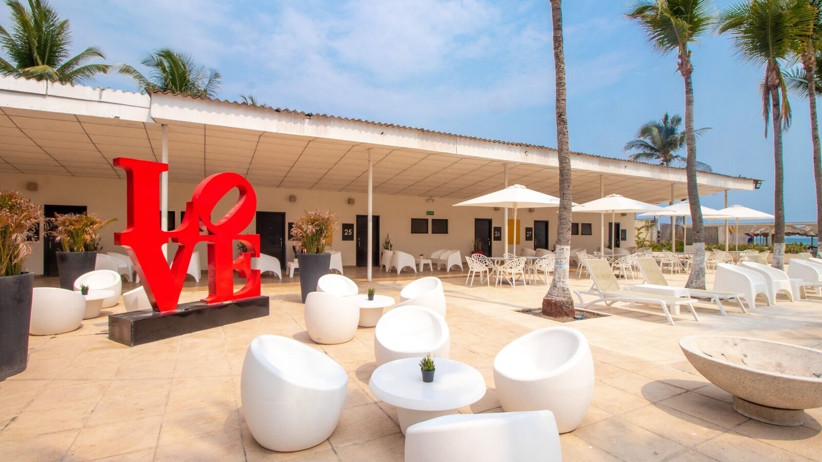 Un complexe hôtelier doté d’une terrasse, de palmiers et d’un grand panneau rouge sur lequel est écrit le mot « AMOUR ».