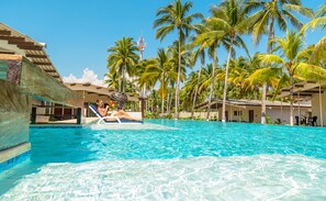 A pool area with clear blue water, surrounded by palm trees and a building with a sloped roof.