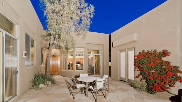 A patio with a stone table and chairs, a tree, and a red flowering bush. - Desert Rose By Signature Vacation Rentals (Scottsdale)
