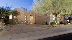 A modern house with a stone facade, a curved driveway, and a well-maintained garden with cacti and a tree. - Desert Rose By Signature Vacation Rentals (Scottsdale)