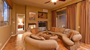 A living room with a sectional sofa, a flat-screen TV, a fireplace, and a ceiling fan. - Desert Rose By Signature Vacation Rentals (Scottsdale)
