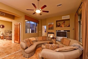 A living room with a curved sectional sofa, a fireplace, a television, and a ceiling fan.