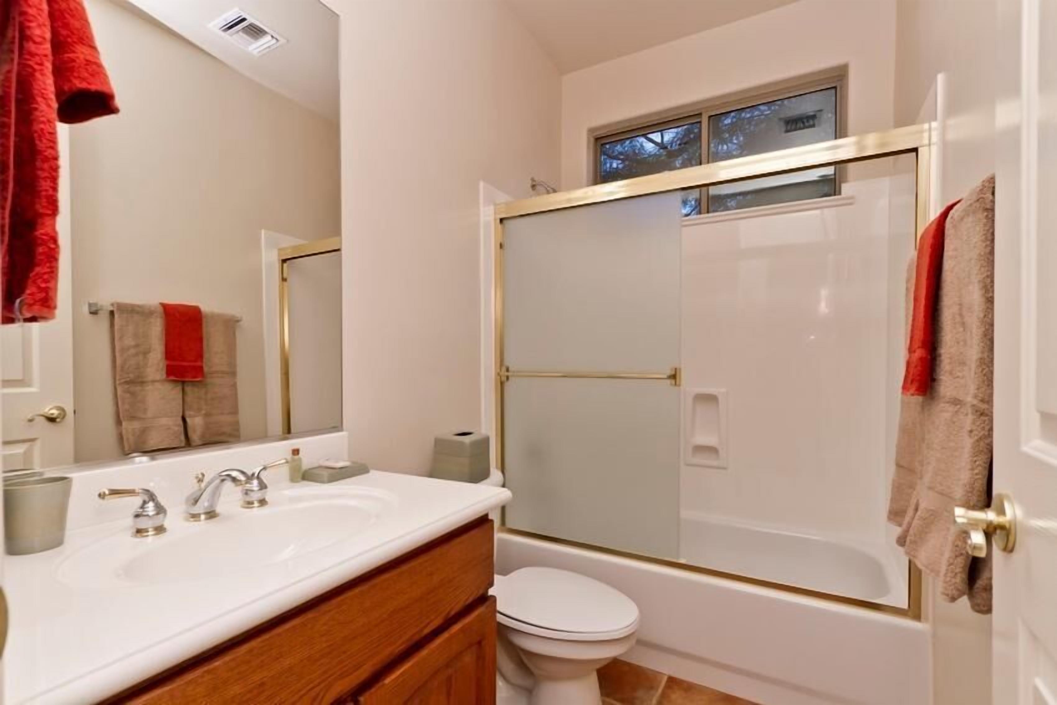 A bathroom with a white sink, two faucets, a mirror, a toilet, and a glass-enclosed shower.
