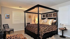 A four-poster bed with a patterned bedspread, a leopard print rug, and a small round table with a lamp.