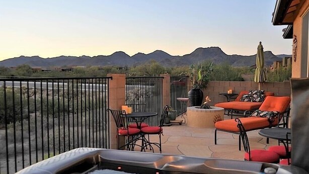 An outdoor patio with a hot tub, orange and black furniture, and a view of mountains.
