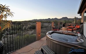 Un jacuzzi en un patio con vistas a las montañas, un área cercada y mobiliario de exterior.