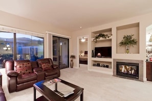 A modern living room with a leather sofa, a fireplace, and a TV mounted on the wall.