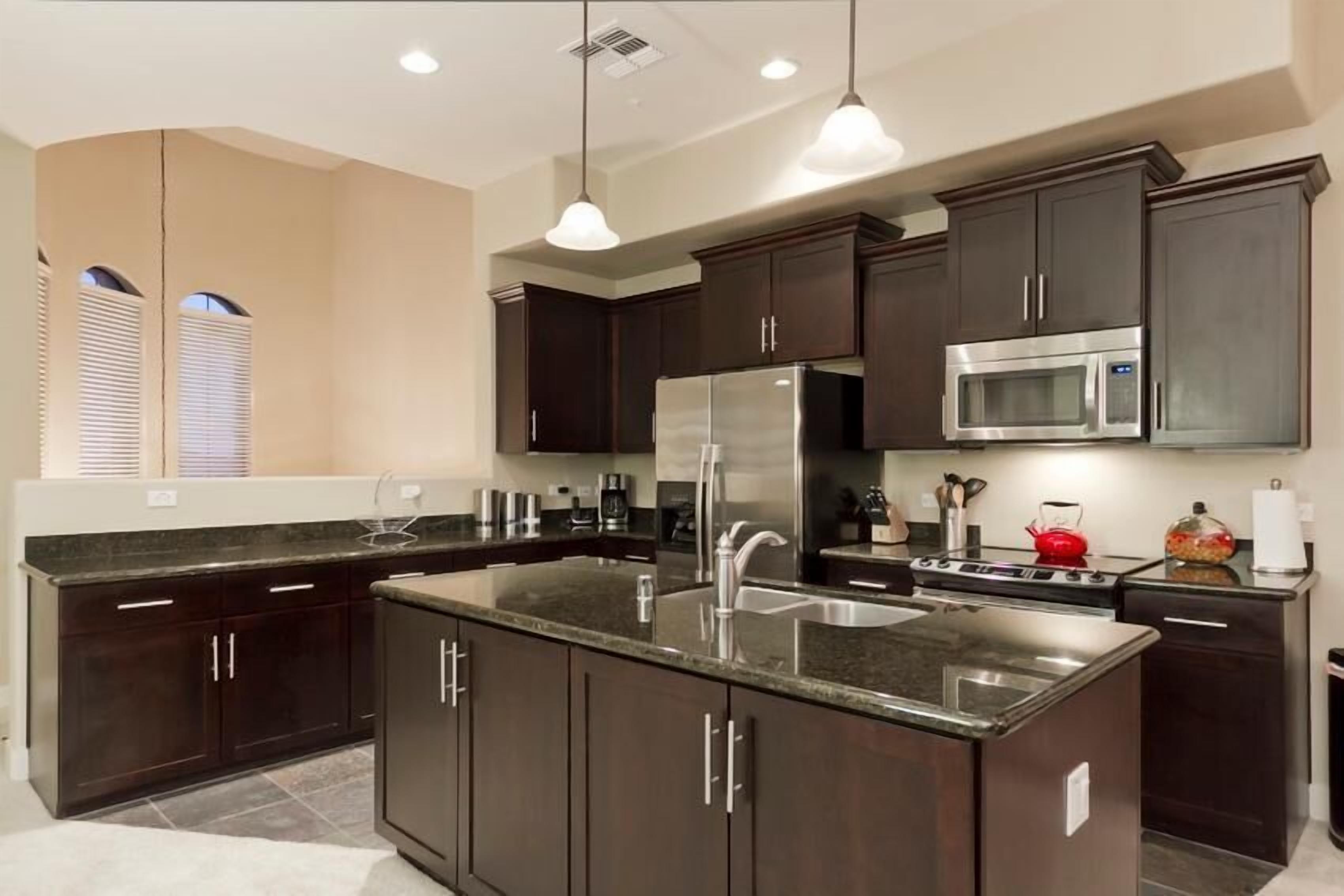 A modern kitchen with dark cabinetry, stainless steel appliances, and pendant lighting.