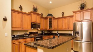 A kitchen with wooden cabinets, granite countertops, stainless steel appliances, and decorative plants. - Desert Falls By Signature Vacation Rentals (Glendale)