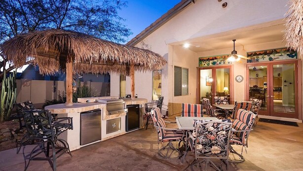 An outdoor kitchen with a grill and seating area. - Desert Falls By Signature Vacation Rentals (Glendale)