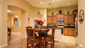 A spacious kitchen with wooden cabinets, a dining area with a table and chairs, and a clock on the wall. - Desert Falls By Signature Vacation Rentals (Glendale)