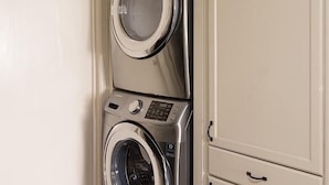 Een kleine wasruimte met een gestapelde wasmachine en droger, een kast met lades en een gestructureerd plafond.