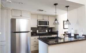 Een moderne keuken met roestvrijstalen apparatuur, een zwart aanrecht en hangende lampen.