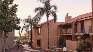 A courtyard with a palm tree, a fountain, and a building with a balcony. - Casita Escriber By Signature Vacation Rentals (Oro Valley)