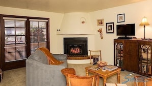 A living room with a fireplace, a television, and a bookshelf. - Casita Escriber By Signature Vacation Rentals (Oro Valley)