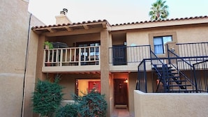 A two-story building with a balcony on the upper floor, a staircase on the right, and a small garden area with plants and a pathway. - Casita Escriber By Signature Vacation Rentals (Oro Valley)