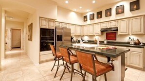 A modern kitchen with white cabinetry, a central island with bar stools, stainless steel appliances, and recessed ceiling lighting. - Casa De Luna By Signature Vacation Rentals (Scottsdale)