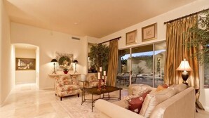 A spacious living room with a beige sofa, a coffee table, and floral armchairs. There are two lamps, a potted plant, and a framed picture on the wall. - Casa De Luna By Signature Vacation Rentals (Scottsdale)