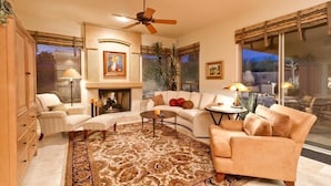 A living room with a fireplace, a ceiling fan, and a large window. - Casa De Luna By Signature Vacation Rentals (Scottsdale)