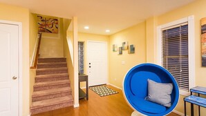 Un couloir avec un escalier, une chaise bleue et une porte.