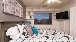 Une chambre à coucher avec un lit, un ventilateur de plafond, une télévision et une fenêtre avec des stores.