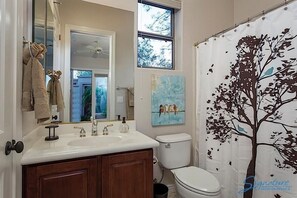 A bathroom with a white sink, two mirrors, a toilet, and a shower curtain with a tree design. - Caledonia Dreamin By Signature Vacation Rentals (Phoenix)