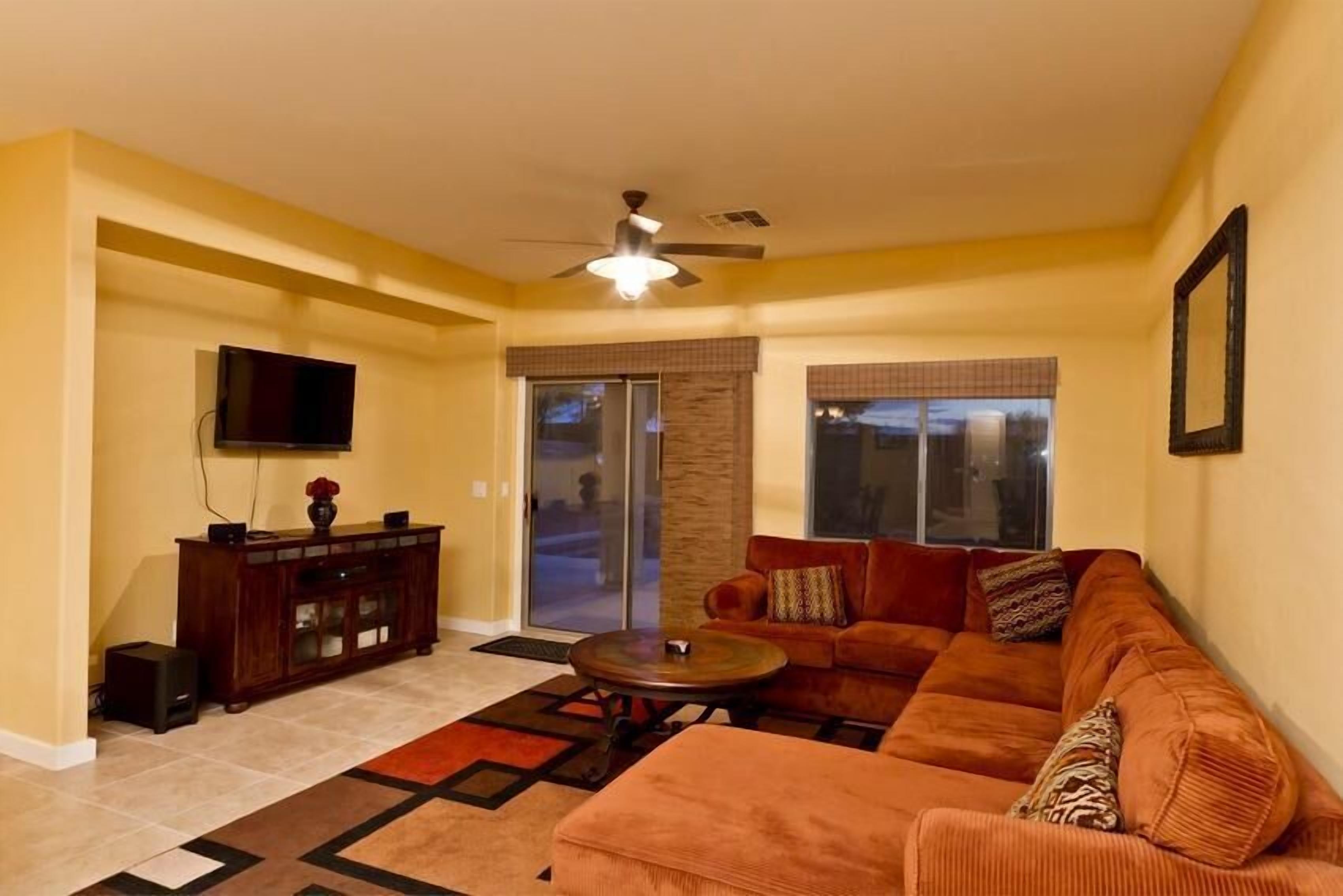A living room with a sofa, coffee table, TV, and a ceiling fan.