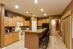 A modern kitchen with wooden cabinets, a central island with bar stools, a refrigerator, and a microwave.