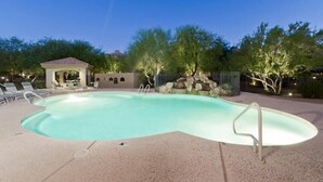 A swimming pool with a curved edge, surrounded by lounge chairs and a small gazebo.
