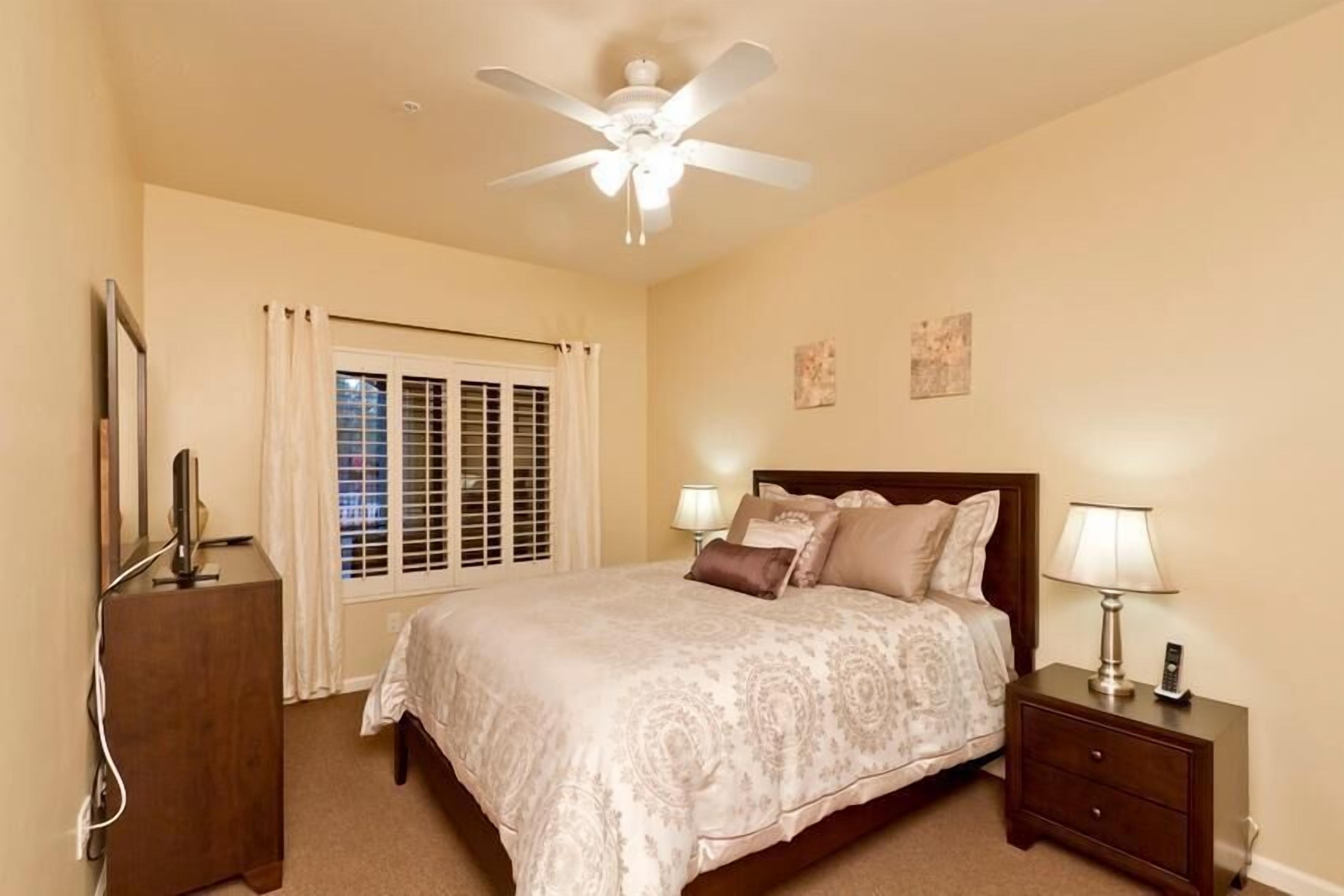 A bedroom with a bed, bedside tables, a ceiling fan, and a window with curtains.