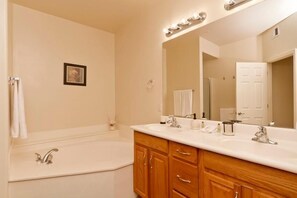 A bathroom with a large mirror, two sinks, a bathtub, wooden cabinets, and a framed picture on the wall. - Bella Vista By Signature Vacation Rentals (Scottsdale)