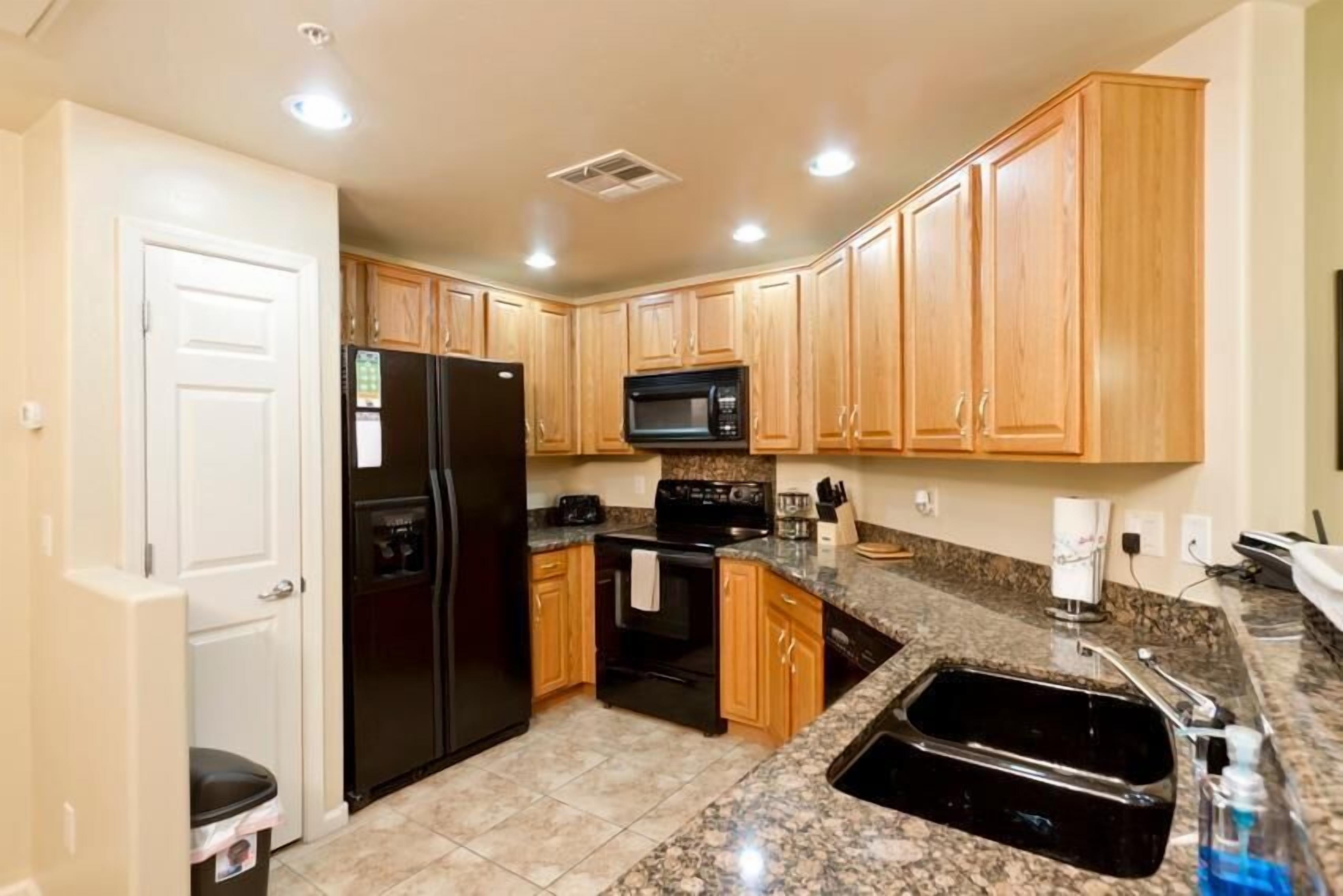 A kitchen with wooden cabinets, a black refrigerator, a microwave, a stove, and a granite countertop sink.