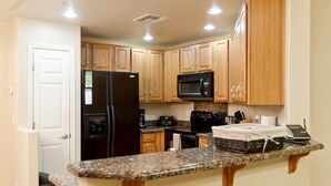 A kitchen with wooden cabinets, a granite countertop, a black refrigerator, a microwave, and a coffee maker.