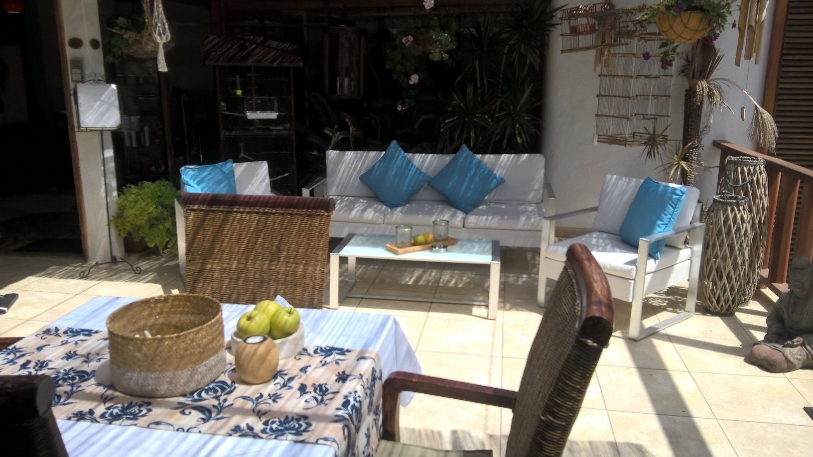 An outdoor seating area with wicker furniture, a table with a bowl of fruit, and a wicker basket.