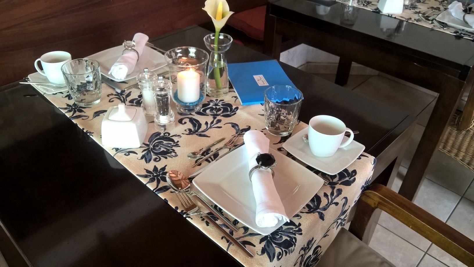 A dining table set with plates, cutlery, glasses, a candle, and a flower.