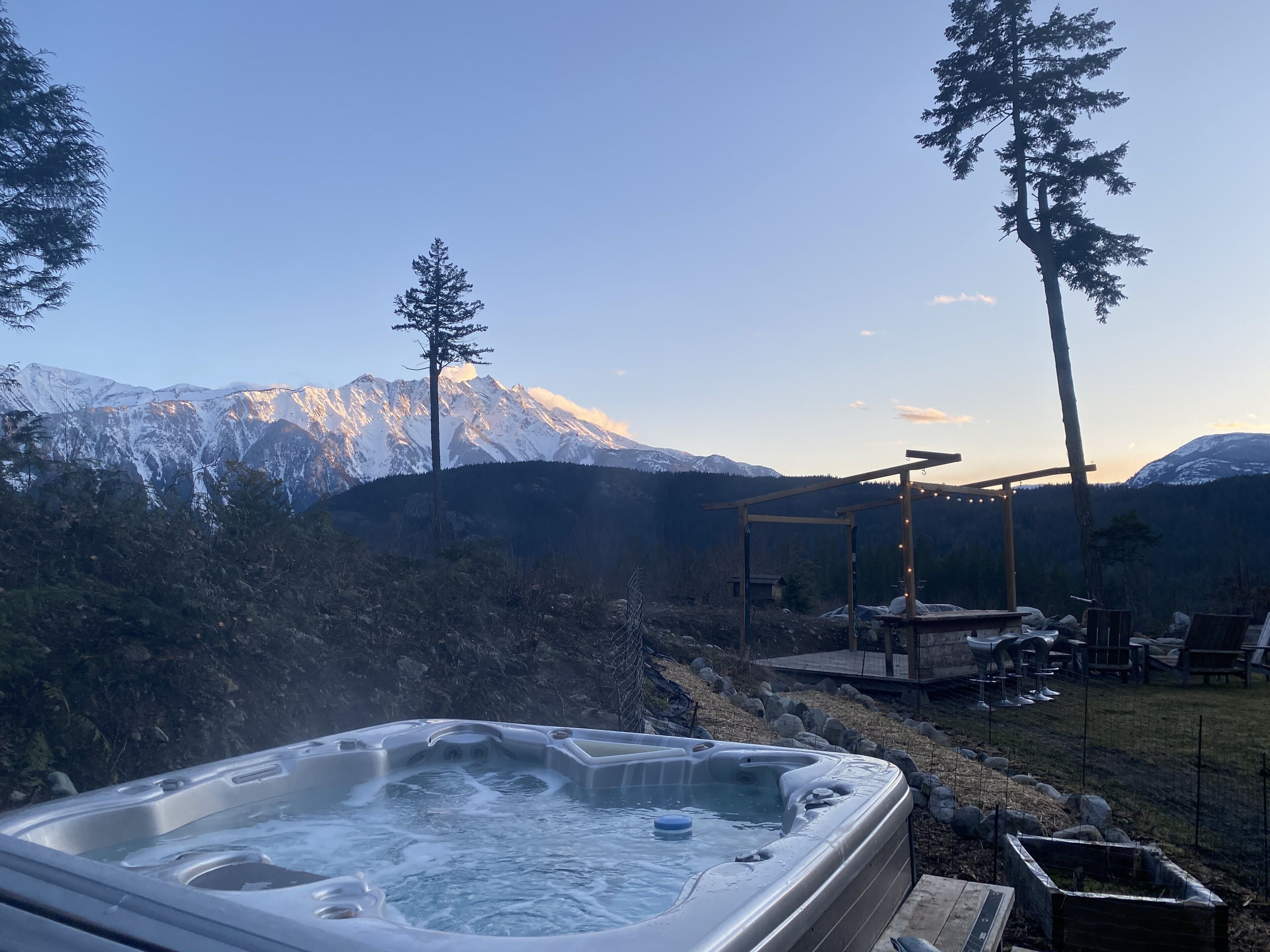 A hot tub with a mountain view, surrounded by trees and a wooden deck.