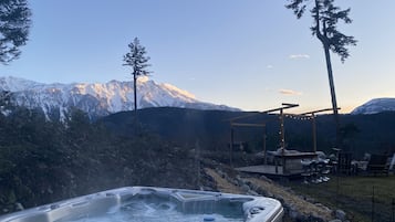 A hot tub with a mountain view, surrounded by trees and a wooden deck.