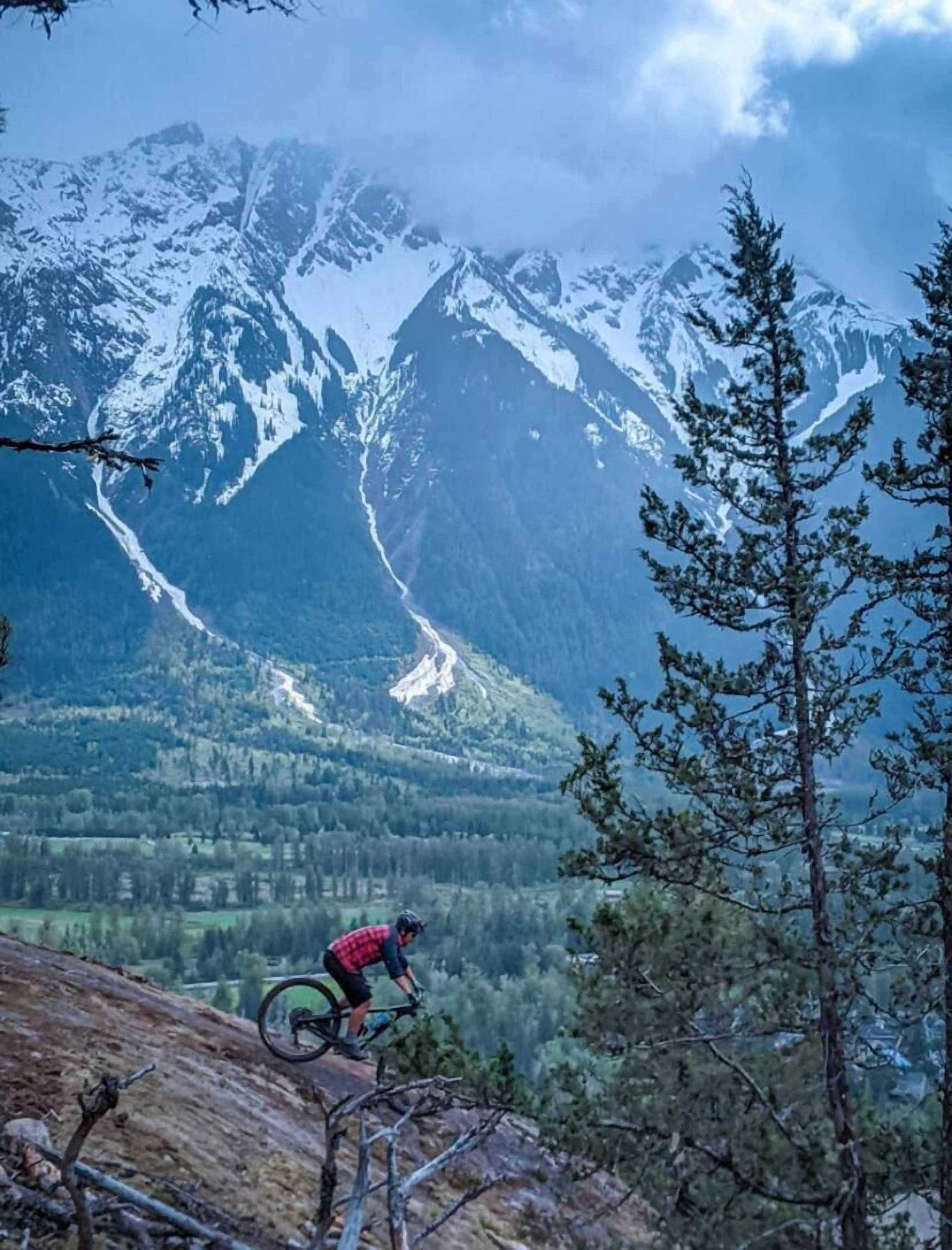 Ein Mountainbiker auf einem Pfad, im Hintergrund schneebedeckte Berge.