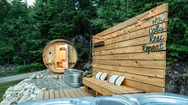 A wooden cabin with a hot tub and a bench, surrounded by a forest. - The Cabin at Sweetwater Lane Farm (Mount Currie)