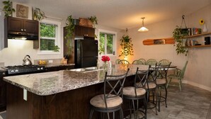 A kitchen with a large island, bar stools, a refrigerator, and a hanging plant. - The Cabin at Sweetwater Lane Farm (Mount Currie)