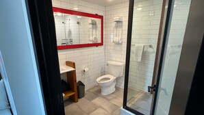 A modern bathroom with white tiles, a glass shower enclosure, a toilet, and a sink with a mirror. - Hotel 1080 Brooklyn (Brooklyn)