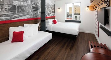 Quarto de hotel com duas camas, piso de madeira, painel de parede com vista para a cidade e televisão montada.