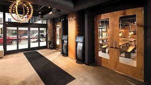A modern interior with a reception area, wooden walls, and a black carpet leading to a seating area with tables and chairs. - Hotel 1080 Brooklyn (Brooklyn)